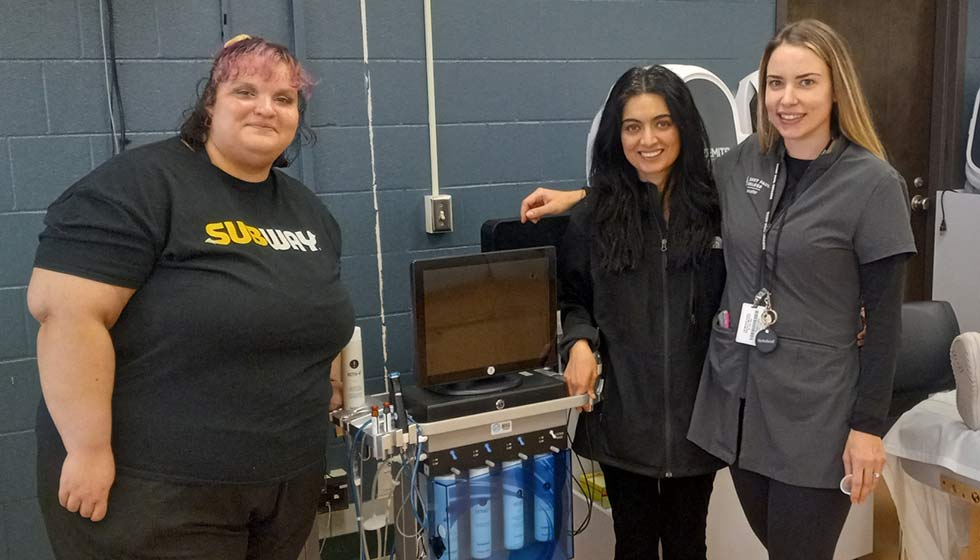 Jessica Velez, Nafia Sikder, and Instructor Margaret Kelly standing by equipment in esthetics lab.